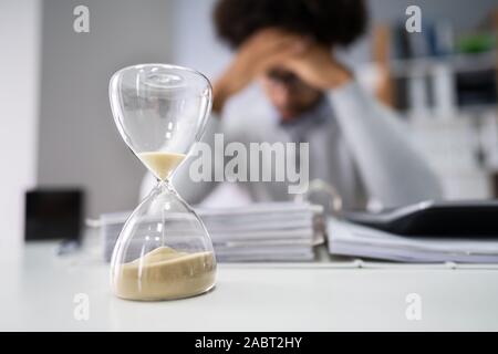 Close-up Of Hourglass In Front Of Businessperson Working In Office Stock Photo