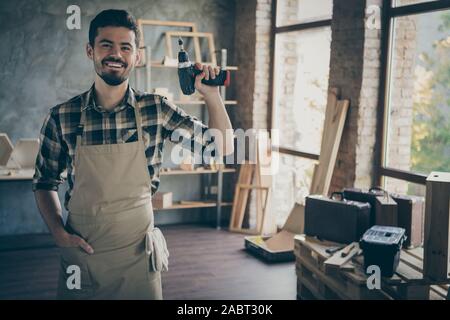 Photo of handsome confident guy master holding electric wireless drill friendly smiling ready to start repair own wooden business industry studio Stock Photo