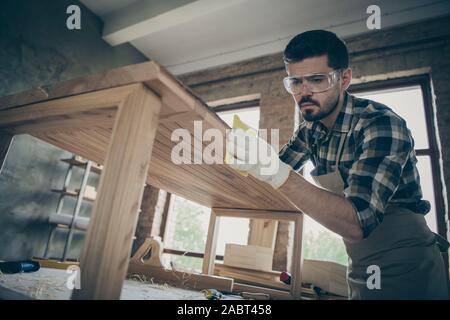 Low angle view photo of concentrated man hardwood worker renew wooden furniture slab table polish smooth surface in home house garage Stock Photo