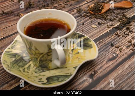 Cup of black tea, tea leaves in a wooden spoon on a wooden background. Close up Stock Photo