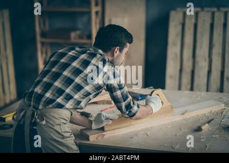 Photo of serious confident back rear view joiner polishing plank to use it for making new furniture in gloves Stock Photo