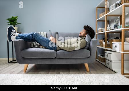 Man Using Digital Tablet Lying In Sofa Stock Photo