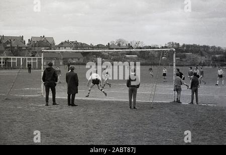 1971, historical, behind the goal net, some spectators watching local football match in a park, England, UK. Stock Photo