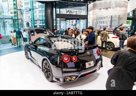 Nissan flagship showroom, Ginza, Tokyo. People viewing the display of a high performance black sports car, the GTR in the main showroom. Stock Photo