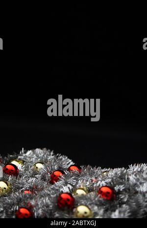 Christmas vertical copy space with red and golden bright baubles in silver decorative chain garland on black background with bokeh effect Stock Photo