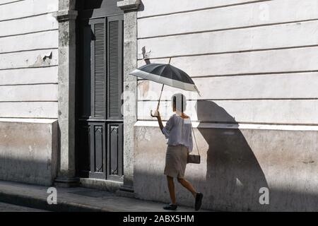 Woman walking with an umbrella to protect her from the sun, Merida, Mexico Stock Photo
