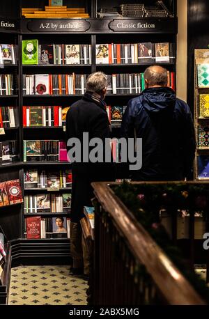 Rear view portrait of two men standing side by side in front of a 'classic fiction' bookshelf, Hatchards bookshop, London, England, UK. Stock Photo