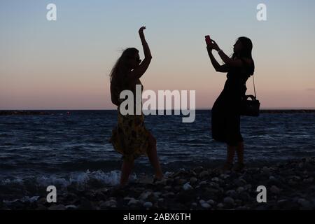 Two young girls from East Europa on beach silhouetted taking pictures with their  smartphones at sunset