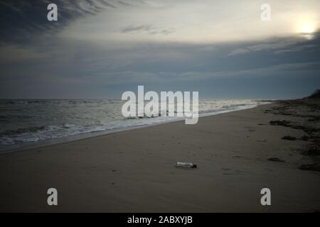 Wild sandy sea beach wirh empty glass bottle on a wet sand. Stock Photo