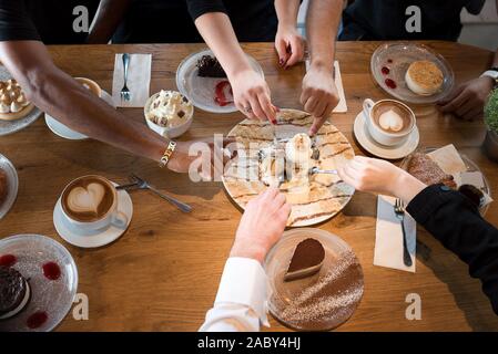 Friends with desserts and coffee, close up.Happy couple sitting around the table and watch football games on TV. Hands holding cups, happy festive moment, luxury celebration concept. Stock Photo