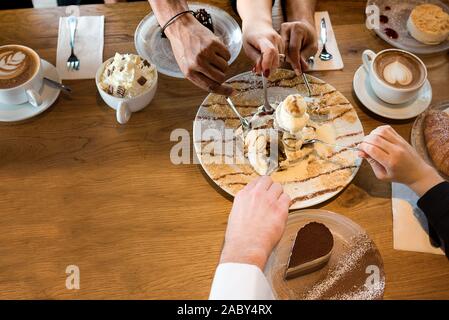 Friends with desserts and coffee, close up.Happy couple sitting around the table and watch football games on TV. Hands holding cups, happy festive moment, luxury celebration concept. Stock Photo