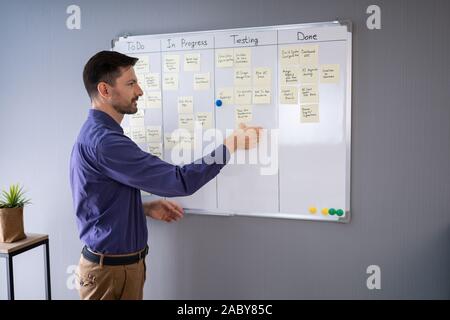 Side View Of Businessman Writing On Sticky Notes Attached To White Board In Office Stock Photo