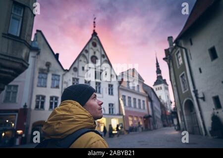 Young man in winter coat walking in historical street at moody sunset. Old town in Tallinn, Estonia.