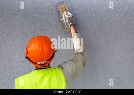 Applying decorative plaster on wall by a steel trowel. White cement based decorative top coat plaster resistant on outside whether conditions. Selecti Stock Photo