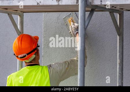 Hand of worker applying decorative plaster on wall by a steel trowel. White cement based decorative top coat plaster resistant on outside whether cond Stock Photo