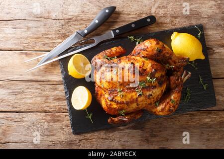 Traditional rotisserie chicken served with lemon closeup on a slate board on a table. Horizontal top view from above Stock Photo