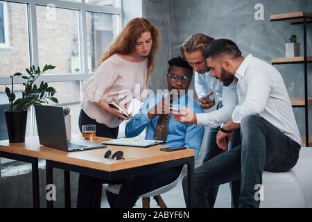 Using smartphone for finding information. Group of multiracial office workers in formal clothes talking about tasks and plans Stock Photo
