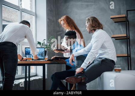 Using laptop. Group of multiracial office workers in formal clothes talking about tasks and plans Stock Photo