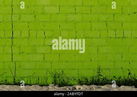 green plaster rough brick wall texture under direct sunlight with snow and dry gasss under Stock Photo