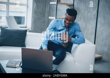 Feeling good. Photo of young afro american guy in glasses and classic wear sitting in a front of laptop Stock Photo