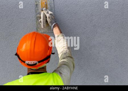 Worker hand applying decorative plaster on wall by a steel trowel. White cement based decorative top coat plaster resistant on outside whether conditi Stock Photo