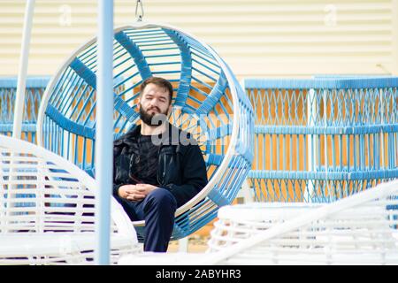 bearded young man has a rest on a swing. guy relaxes on the sun Stock Photo
