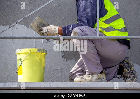 Worker hand applying decorative plaster on wall by a steel trowel. White cement based decorative top coat plaster resistant on outside whether conditi Stock Photo