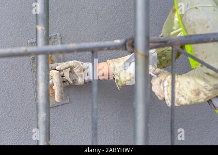 Worker hands applying decorative plaster on wall by a steel trowel. White cement based decorative top coat plaster resistant on outside whether condit Stock Photo