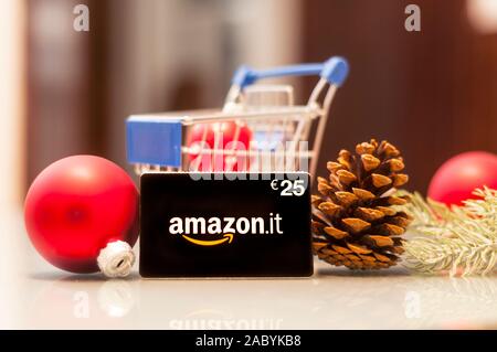 Carrara, Italy - November 29, 2019 - A 25 euro Amazon gift card on a glass table with a shopping cart and some Christmas decorations. The gift card al Stock Photo