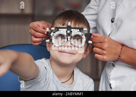Kid smiling and raising hand while undergoing eye test with phoropter Stock Photo
