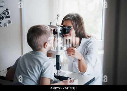Doctor is smiling. Little boy having test for his eyes with special optical apparatus by female doctor Stock Photo