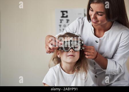 Cheerful atmosphere. Doctor checking little girl sight and tuning the phoropter Stock Photo