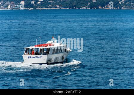 White ferry boat with some tourists sailing in the blue Mediterranean sea in front of the ancien village of Tellaro, Gulf of La Spezia, Italy Stock Photo