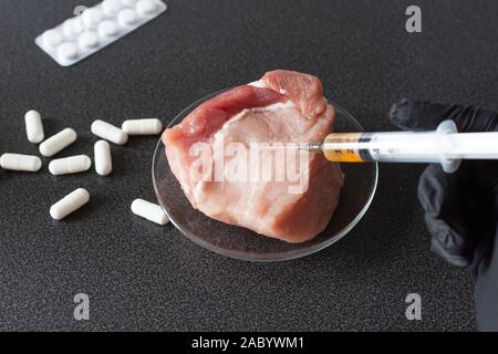 Researcher injecting GMO a slice of pork meat. Genetically modified organism, harmful for peples health. Meat with antibiotics concept. Stock Photo