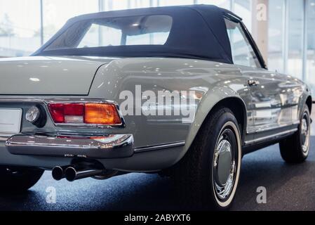 Back and side view of grey retro cabriolet car with close up of right chrome backlight and exhaust pipe, wheel arch above a whitewall tire indoor Stock Photo