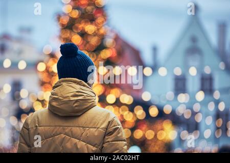 Rear view of man in warm clothing during walk in city. Christmas tree and decoration in Old Town in Tallinn, Estonia.