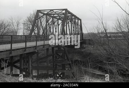 1980s, historical, a wooden bridge with metal enclosed section or span over a small river in the rural Mid-West of America. Known as truss bridges, the early ones used fitted timber beams as the main deck structure with added steel struts grouped in triangular form to support the bridge. Truss bridges come in many different designs. Stock Photo