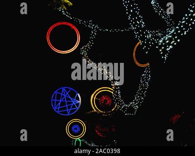 Colorful street christmas lights. Circles in red blue and gold and branches of trees which are surrounded by white fairy lights. Exemption on a black Stock Photo