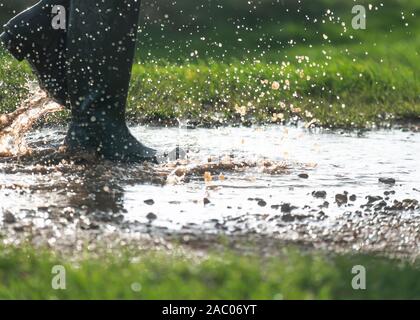 person in green wellington boots having walking in a large muddy puddles in the early morning light  copy space to side of image Stock Photo