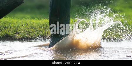 man or lady in green wellington boots walking in a large muddy puddle in the sunshine of the early morning light  copy space to side of image Stock Photo