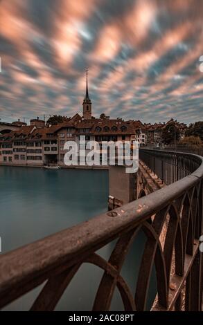 Long exposure of dramatic sunset sky clouds with focus on bridge hand railing and river Aare in Bern, UNESCO, Switzerland Stock Photo