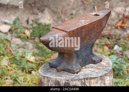Old rusty anvil on a wooden stump. Blacksmith, metalsmith, farrier tools. Close view. Stock Photo