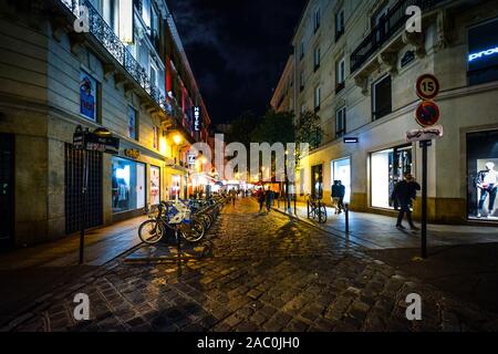 Tourists enjoy a late night walk on a colorful, lively street illuminated by cafe and shop lights in the Latin Quarter district of Paris France. Stock Photo