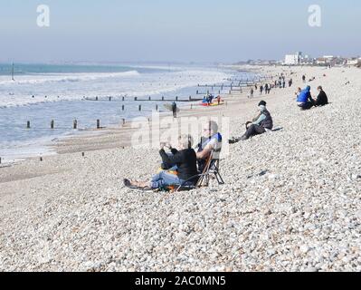 Winter surfing at Selsey beach in February 2019 with people sitting on the beach watching, sea groins in the background Stock Photo