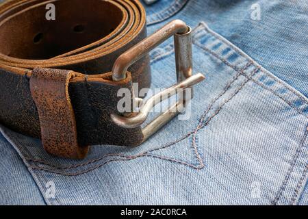 Rolled brown leather belt with metal buckle on blue jeans close-up Stock Photo