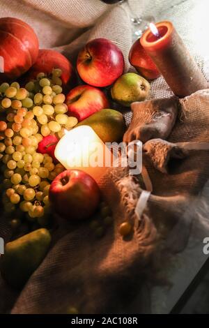 Autumn fruits and vegetables still life on a sackcloth. White grapes sultana red apples and green pears with candles Stock Photo