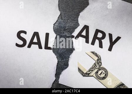 A sheet of white paper with the words salary, torn in half. Low wages require regulation Stock Photo