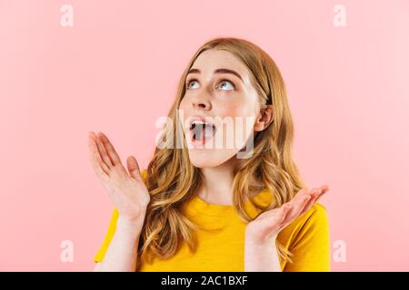 Photo of a young surprised emotional cute girl isolated over pink wall background looking aside. Stock Photo