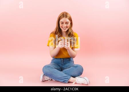 Photo of a young cheerful girl isolated over pink wall background using mobile phone. Stock Photo