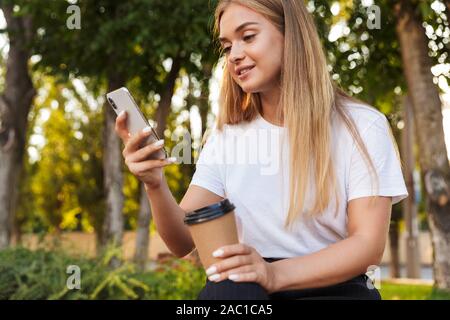Photo of optimistic young lady sit in nature park using mobile phone drinking coffee. Stock Photo